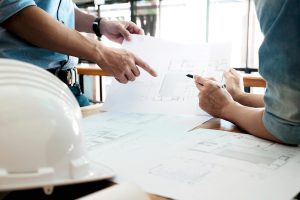 Two professionals reviewing architectural blueprints at a table with a white hard hat.