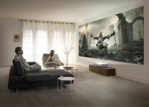 Living room with a couple relaxing while an ultra-short-throw projector displays a knight in armor amid castle ruins on the screen.